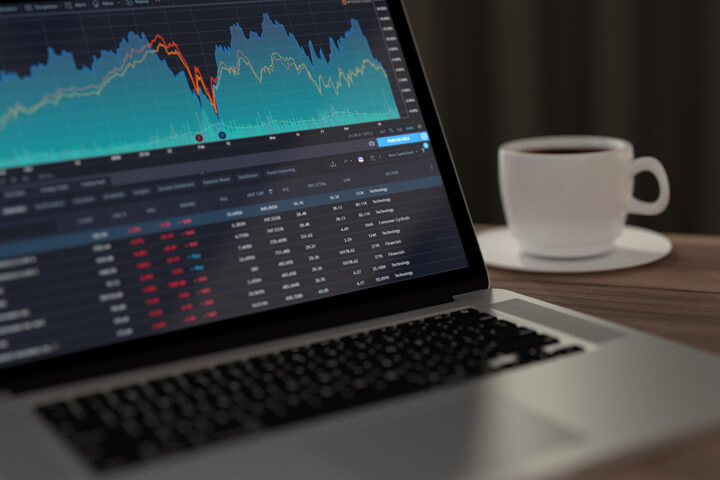 Laptop on table with coffee mug showing stock price information and area chart