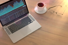 Laptop with stock price screen on table with glasses and coffee cup with lighting flare effect