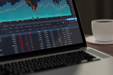 Laptop showing stock prices and area chart with coffee cup in background