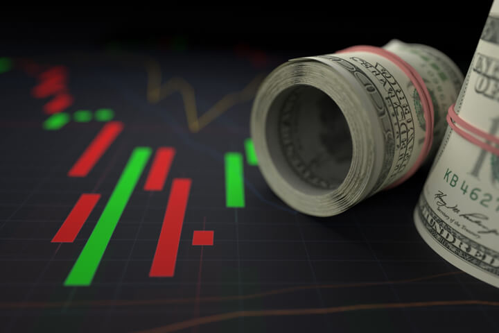 Close up view of rolls of money next to bright stock price candlestick chart