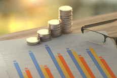 Paper showing investment return column chart with increase stacks of quarters and reading glasses