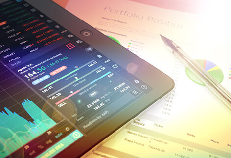 iPad on table showing stock trading data with pen and pie chart on paper
