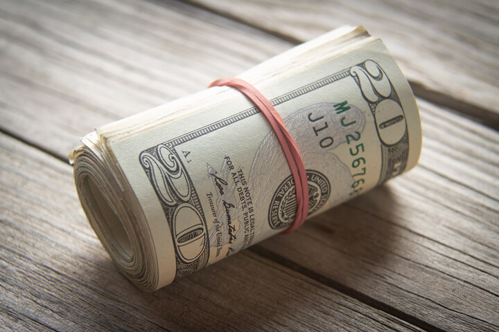 Roll of 20 dollar bills with rubber band on wood background