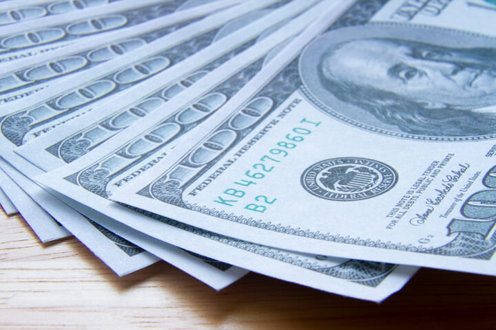 $100 bills evenly fanned out on wood with hard shadow