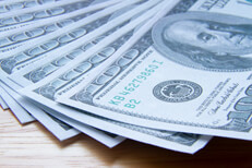 $100 bills evenly fanned out on wood with hard shadow