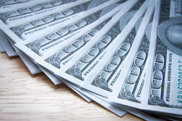 $100 bills evenly fanned out on wood table