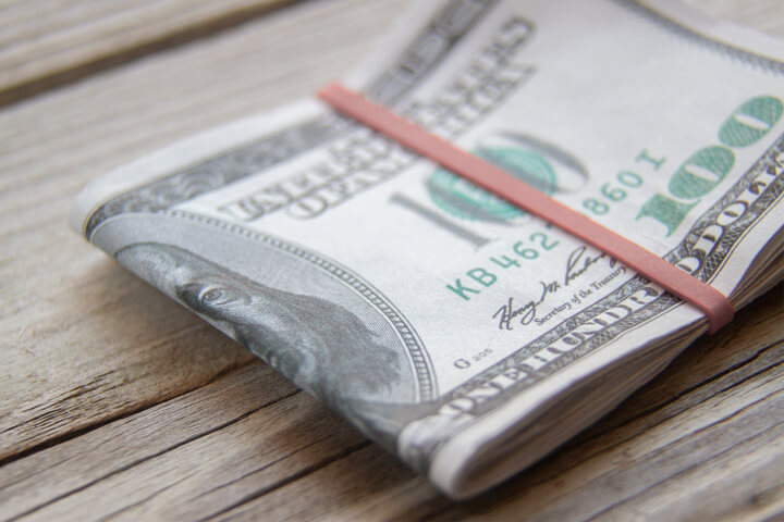 $100 bills folded with rubber band on weathered wood background