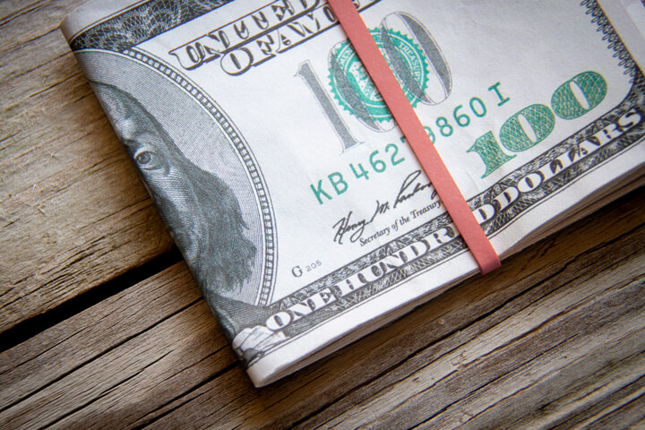 $100 bills folded with rubber band on weathered wood background top view