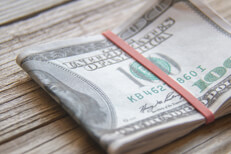 $100 bills folded with rubber band on weathered wood background