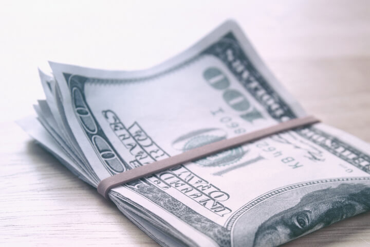 $100 bills folded with rubber band on wood table