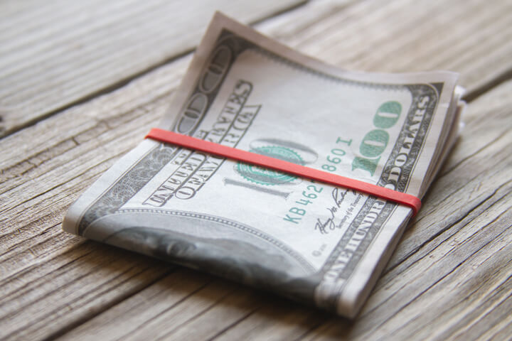 $100 bills folded with rubber band on weathered wood planks