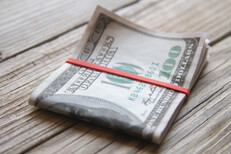 $100 bills folded with rubber band on weathered wood planks