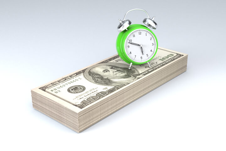 Clock sitting on stack of money concept image for time is money, time value of money, or retirement