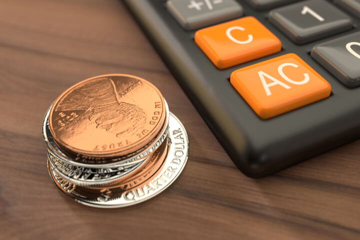 Stack of coins next to calculator on wood table top