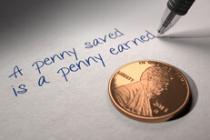 U.S. penny on paper with pen writing A penny saved is a penny earned