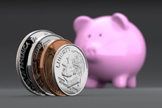 U.S. coins standing on edge in foreground with blurred pink piggy bank in background