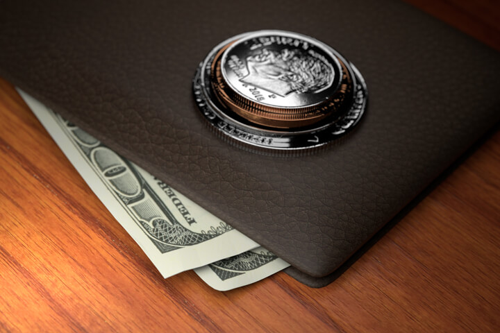 U.S. coins stacked on top of leather wallet with protruding one hundred dollar bills