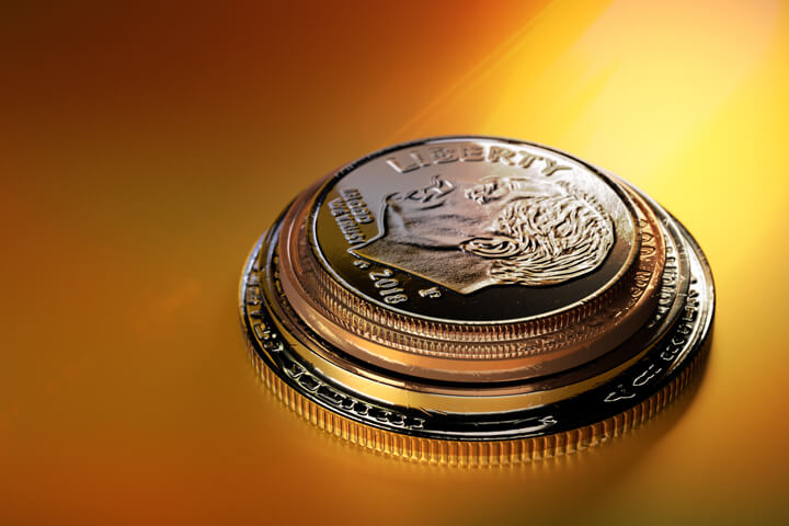Stacked penny, nickel, dime, and quarter on orange background with strong yellow lighting