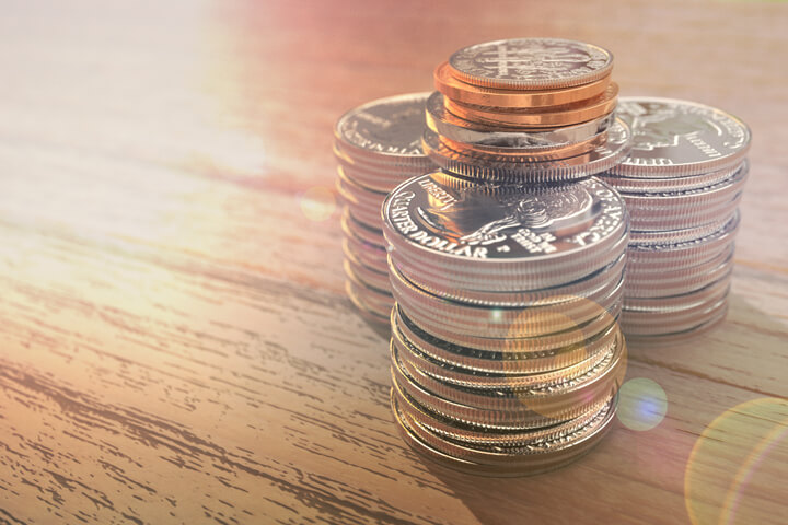 Three large stacks of shiny quarters with other smaller coins on top with lens flare