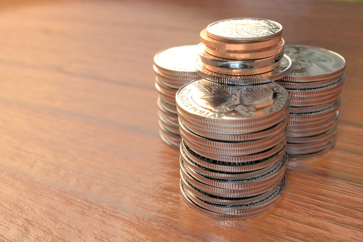 Three large stacks of shiny quarters with other smaller coins on top with rich wood surface