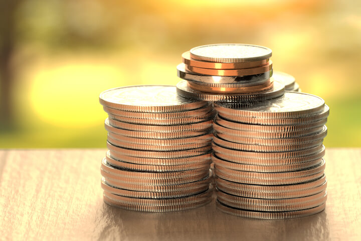 Large stacks of U.S. coins on wood table with sunny yard in background outside window