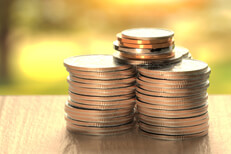 Large stacks of U.S. coins on wood table with sunny yard in background outside window