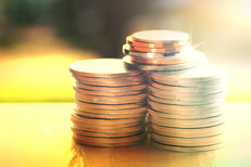 Large stacks of U.S. coins on wood table with sunny yard in background outside window with corner flare and overlay