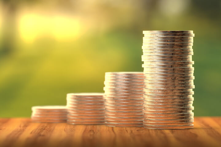 Stacks of coins in front of sunny window increasing like a bar chart to show investment returns over time angled toward camera