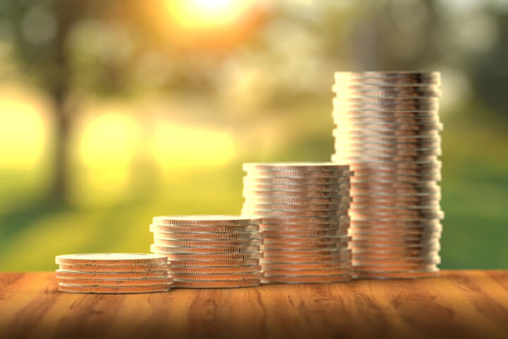 Stacks of coins in front of sunny window increasing like a bar chart to show investment returns over time angled away from camera