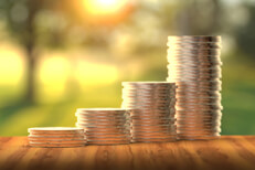 Stacks of coins in front of sunny window increasing like a bar chart to show investment returns over time angled away from camera