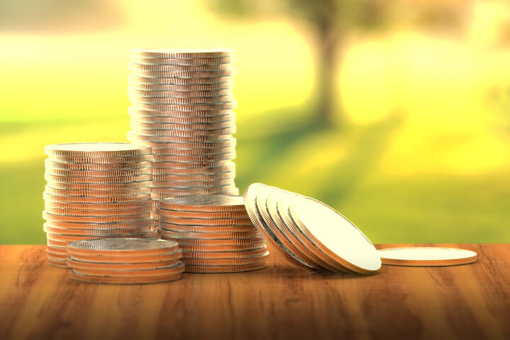 Four different size stacks of coins with some leaning with sunny grass in background