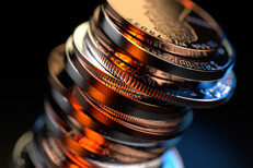 Large stack of U.S. coins on black background with sharp orange and blue contrasting lighting at camera angle