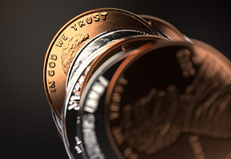 Stack of U.S. coins with focus on penny and hard light on In God We Trust