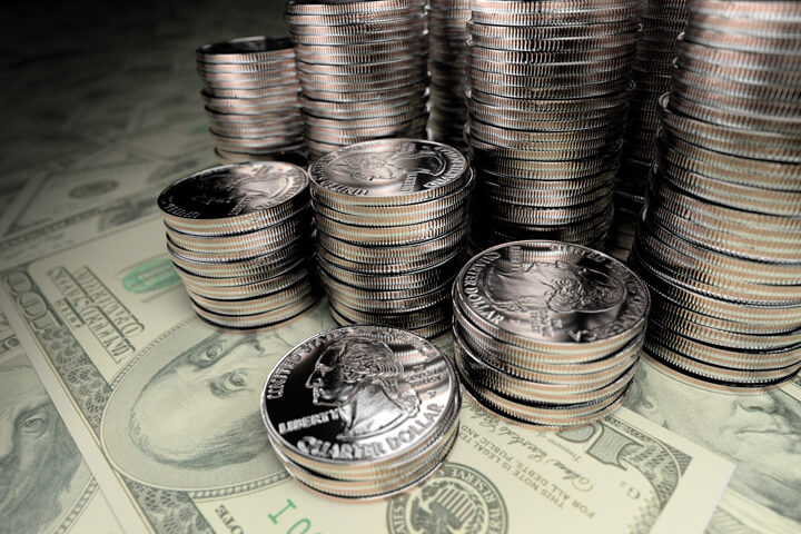 Many stacks of U.S. quarters of different height on one hundred dollar bills