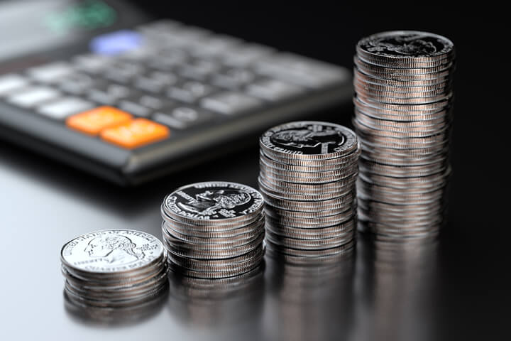 Four increasing stacks of U.S. quarters in front of calculator on black reflective background