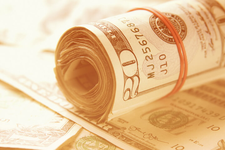 Roll of twenty dollar bills on random stack of bills with bright summer light