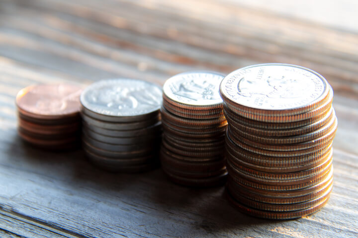 Stacks of pennies, nickels, dimes, and quarters on wood planks in warm morning light