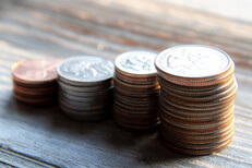 Stacks of pennies, nickels, dimes, and quarters on wood planks in warm morning light