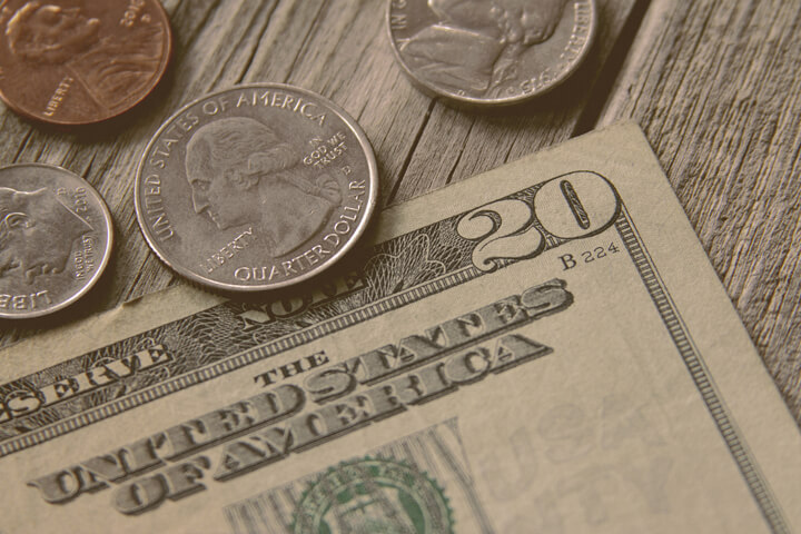 Single twenty dollar bill with quarter, nickel, penny, and dime on wood background