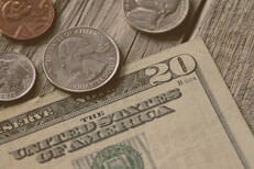 Single twenty dollar bill with quarter, nickel, penny, and dime on wood background