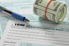 Bundled roll of 100 dollar bills on top of IRS form 1040 with ballpoint pen