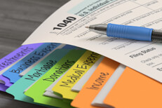 Photo of IRS form 1040 lying on colorful tax folders containing income, expenses, and donations paperwork and receipts