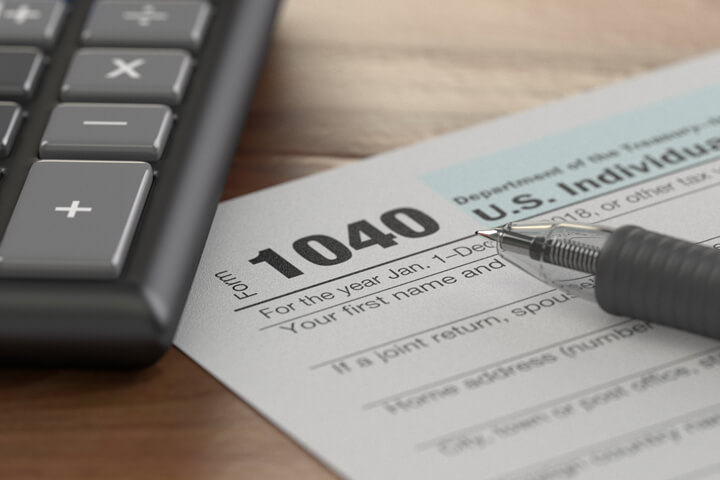 Tax form 1040 with ballpoint pen and calculator on wood surface