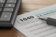 Tax form 1040 with ballpoint pen and calculator on wood surface