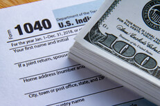 Large bundle of 100 dollar bills on IRS form 1040 concept for paying high taxes