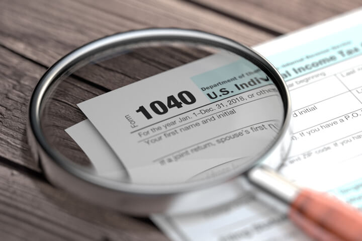 IRS form 1040 lying on worn wood planks with magnifying glass focused on Form 1040 paperwork text