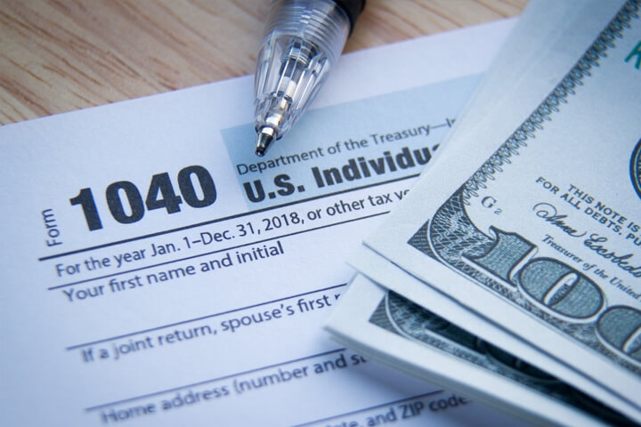 IRS form 1040 with stack of 100 dollar bills and ballpoint pen