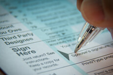 Vignetted close up photo of signature with ballpoint pen on IRS tax form
