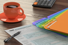Tax prep desk scene Desk with tax folders, 1040 form, calculator, and coffee lit by background window light