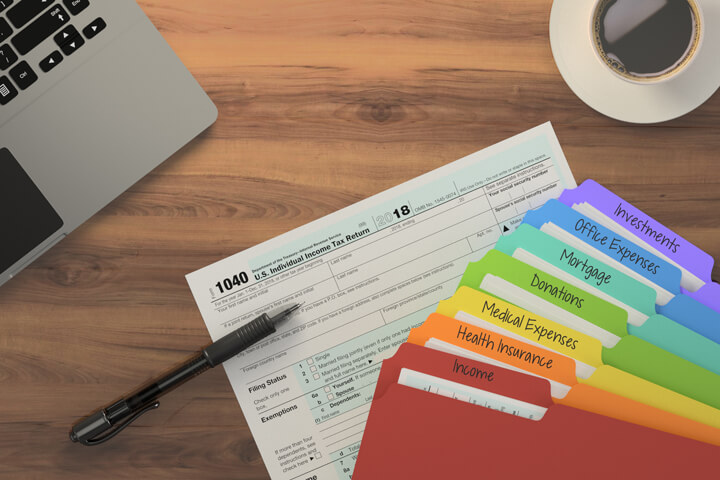 Overhead desk view of laptop, coffee, 1040 form, and rainbow-colored tax category folders